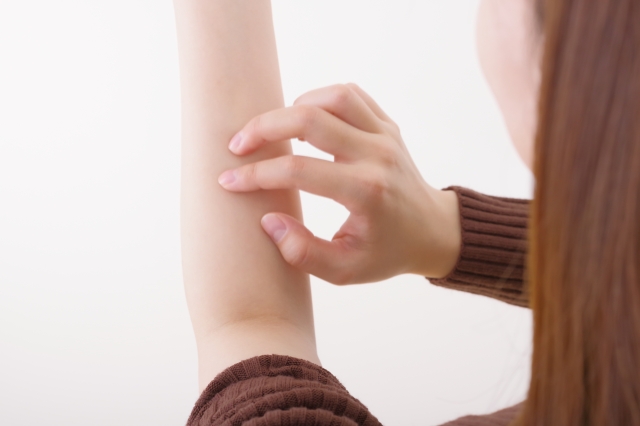 腕の皮膚を引っ掻く女性